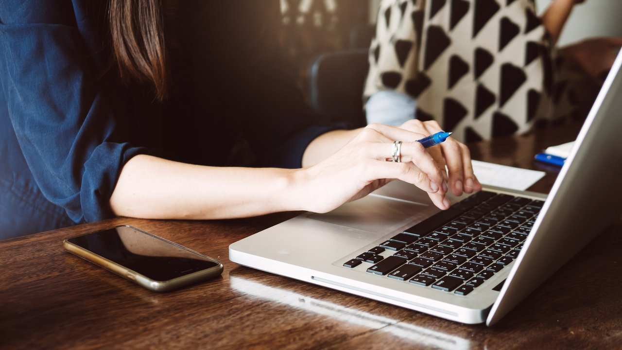 Woman sits at computer with phone Woman sits at computer with phone