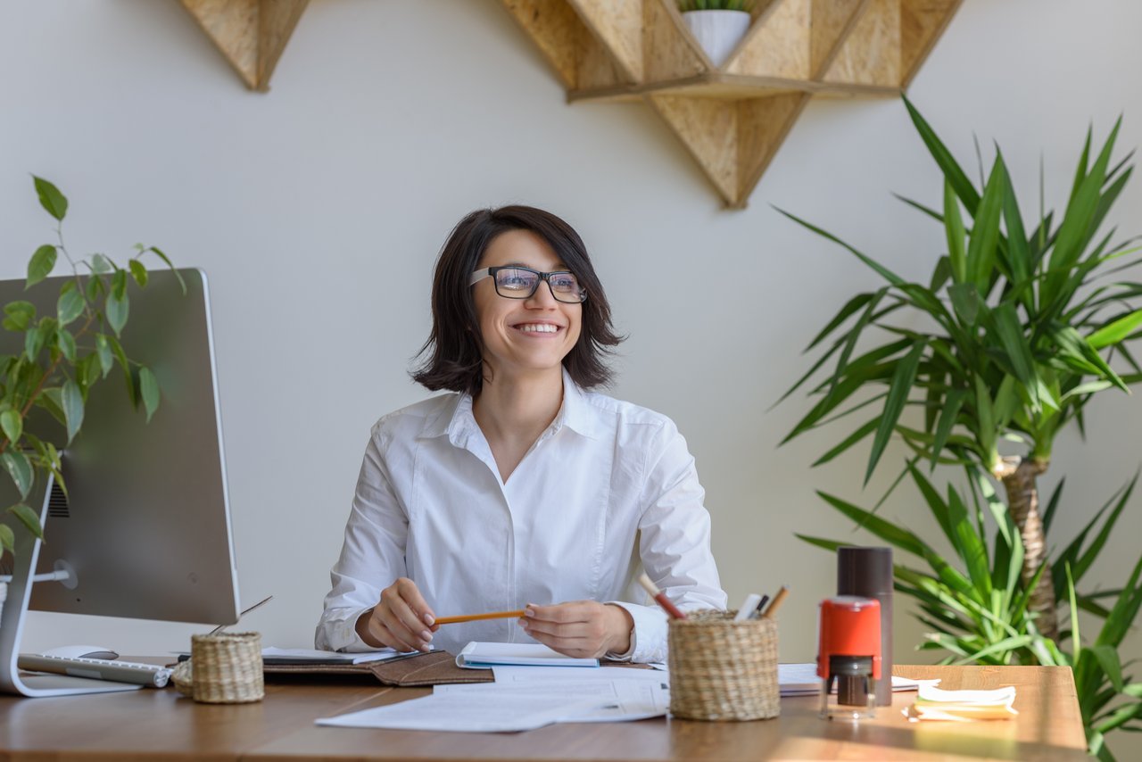 Woman Smiling Sitting at Desk with Plants Woman Smiling Sitting at Desk with Plants